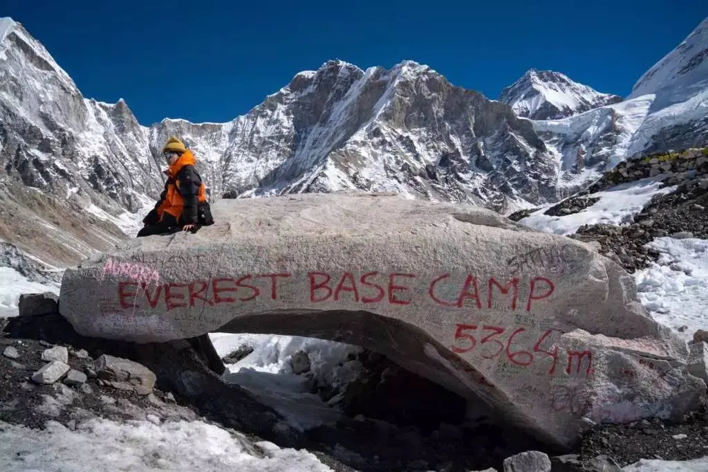 A trekker sitting on the Everest Base Camp rock marked “Everest Base Camp 5364m,” , during Everest Base Camp Trek 13 days