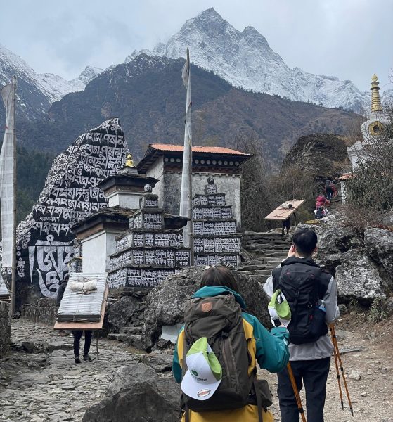 Trekkers, walking up stone steps near prayer walls and a monastery gate, during Everest Base Camp Trek