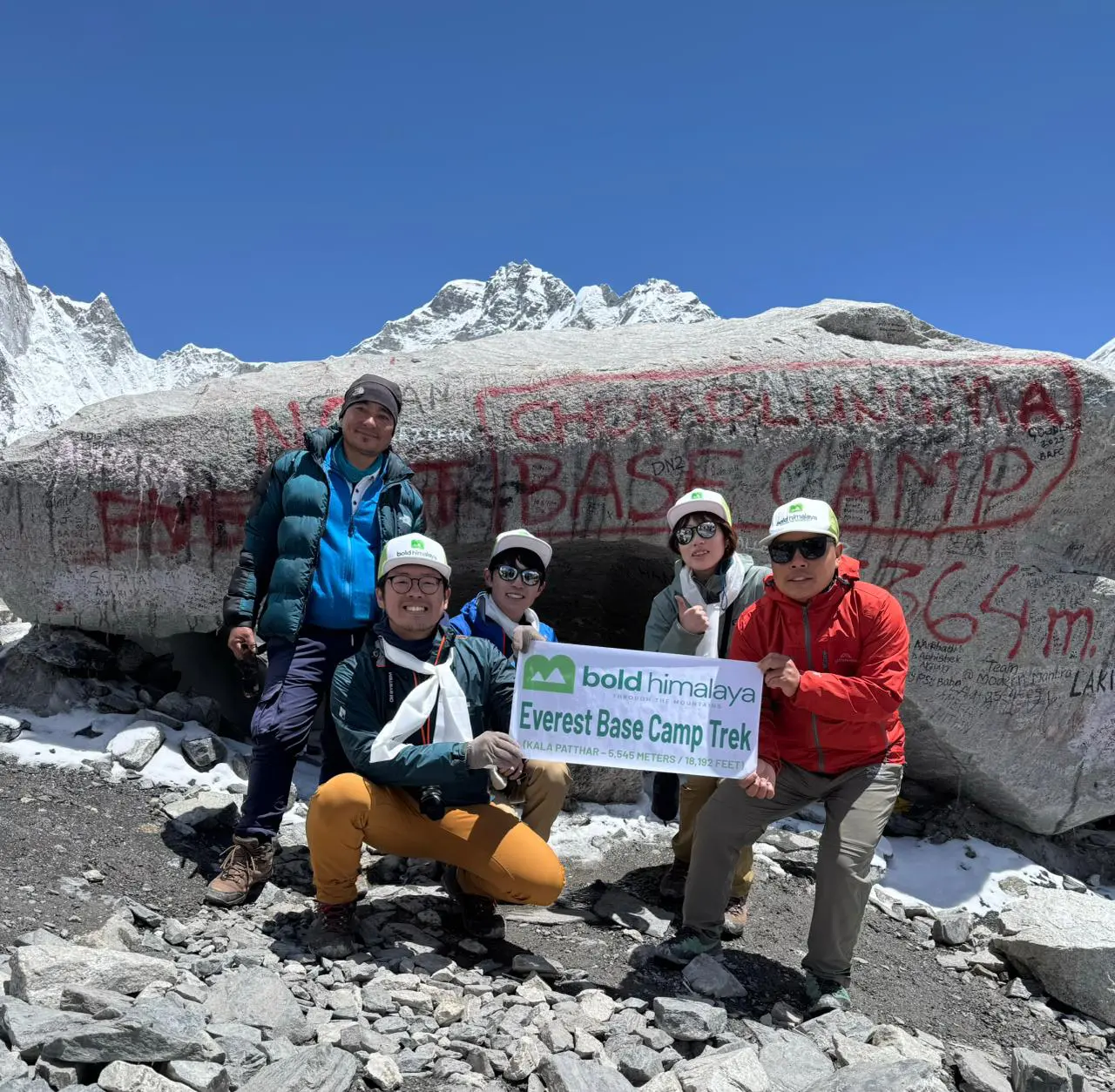 Celebrating success at Everest Base Camp with the company banner, surrounded by the majestic Himalayas, during the Everest Base Camp Trek 14 days