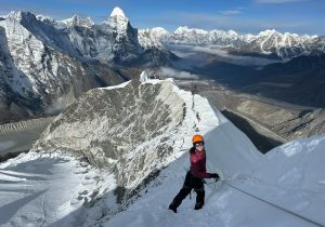 Climber nearing the summit of Island Peak with panoramic mountain views.