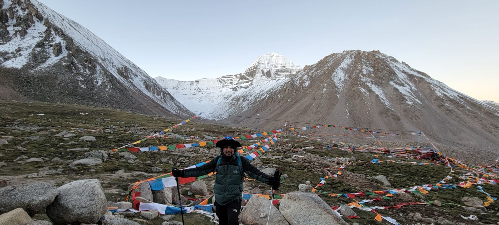 Kailash Charan Sparsh Tour trekker standing near Mount Kailash, north face with prayer flags and a rocky high-altitude landscape
