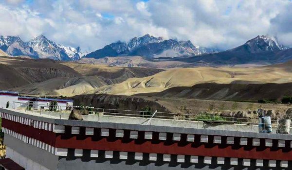 Tibetan-style building with snow-capped mountains in the background on Mount Kailash Mansarovar Tour via Hilsa