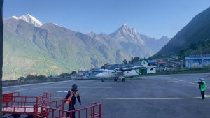 Aircraft standing on the short runway at Lukla Airport with mountain landscape in the background.