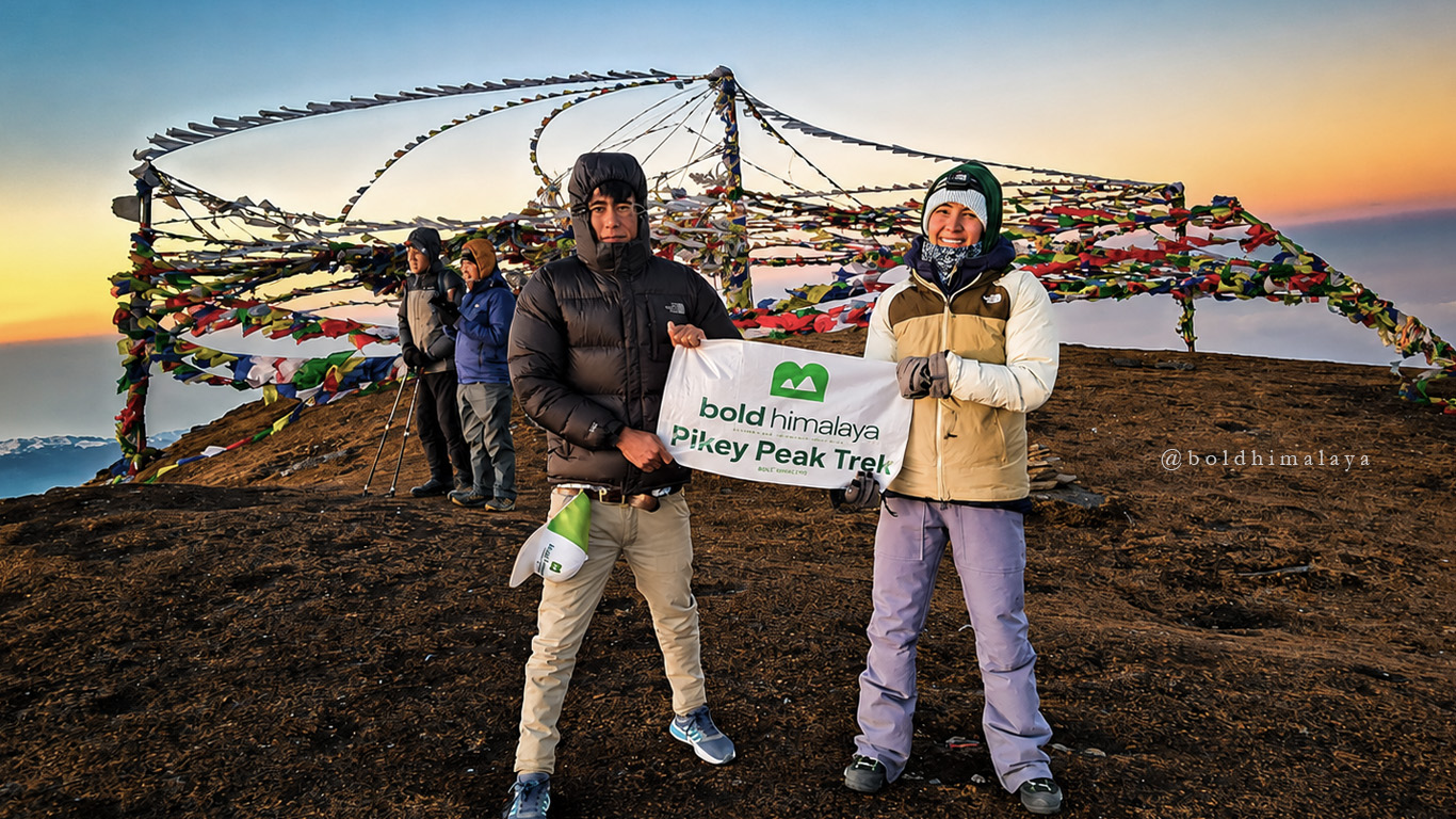 Trekkers holding a banner at Pikey Peak with colorful prayer flags fluttering in the background, during Pikey Peak Trek.