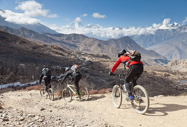 Group of cyclists riding downhill on a rocky trail with snow-capped mountains during the Annapurna Circuit Mountain Biking Trip.