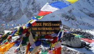 Larke Pass sign at 5106 meters on the Manaslu Circuit with colorful prayer flags and snowy Himalayan peaks.