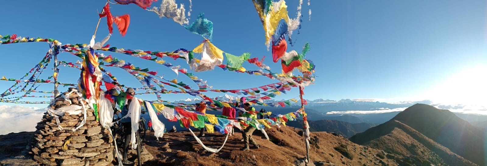 Colorful prayer flags fluttering at the Pikey Peak viewpoint with a wide Himalayan mountain panorama.