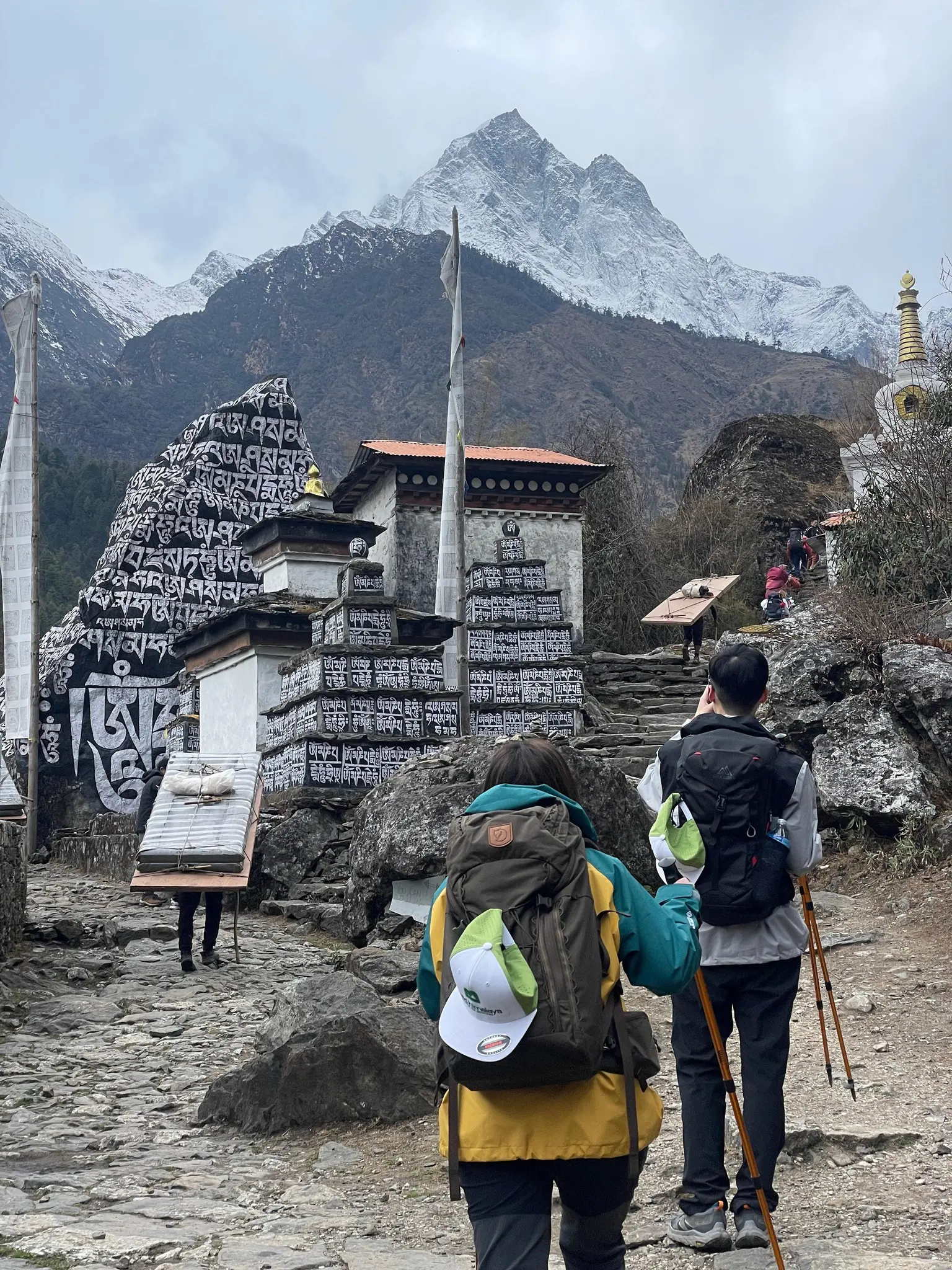 Trekkers walking past mani walls and chortens near Tengboche Monastery during the Everest Base Camp Trek in Nepal.