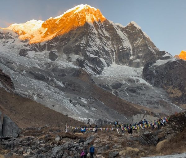 Trekkers at Annapurna Base Camp with colorful prayer flags fluttering below the golden glow of Mount Annapurna at sunrise and best base camp
trek in Nepal