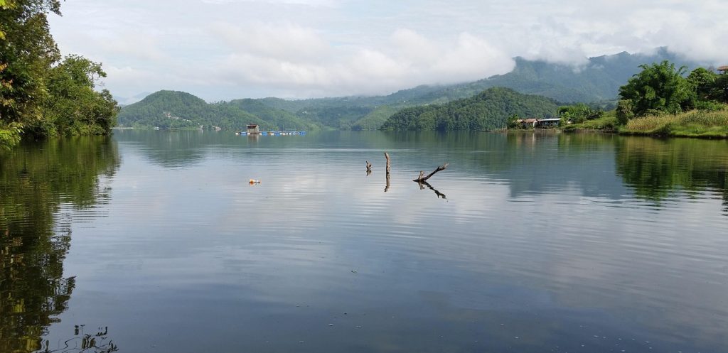Peaceful view of Begnas Lake surrounded by green hills and floating boats, one of the top places to visit in Pokhara