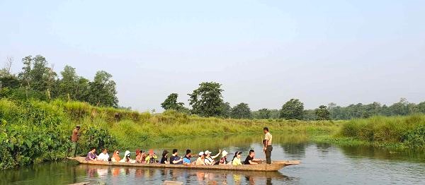 Tourists enjoying a canoe ride during jungle safari tours in Nepal, gliding through a calm river surrounded by lush green forest