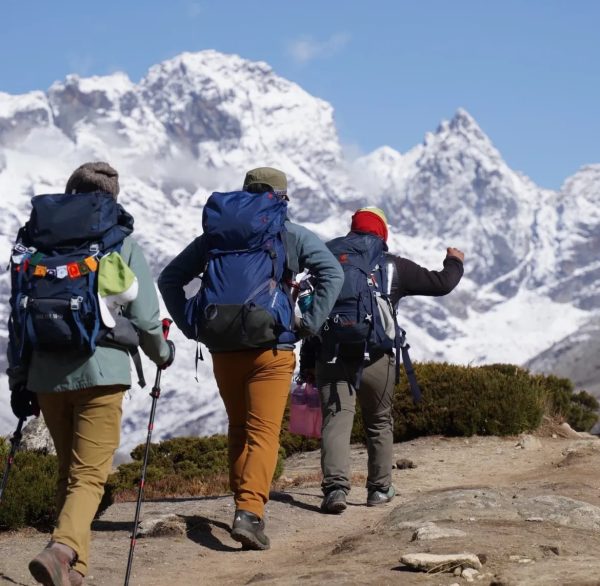 Three trekkers with backpacks walking along a mountain trail toward the snowy peaks of the Everest region during the Everest Base Camp trek