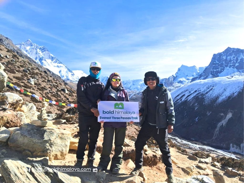 Three trekkers standing at a snowy mountain pass holding a banner during the Everest Three Passes Trek, one of the best high pass treks in Nepal
