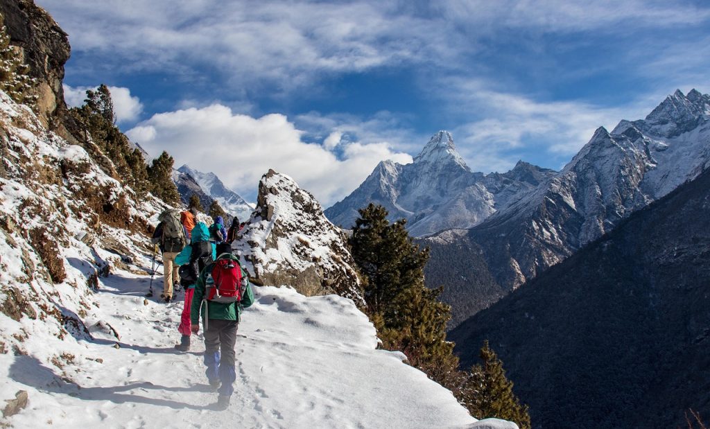 Trekkers walking along a high-altitude Himalayan trail with snow-capped peaks in the background, showcasing an adventure highlighted in the Nepal travel guide
