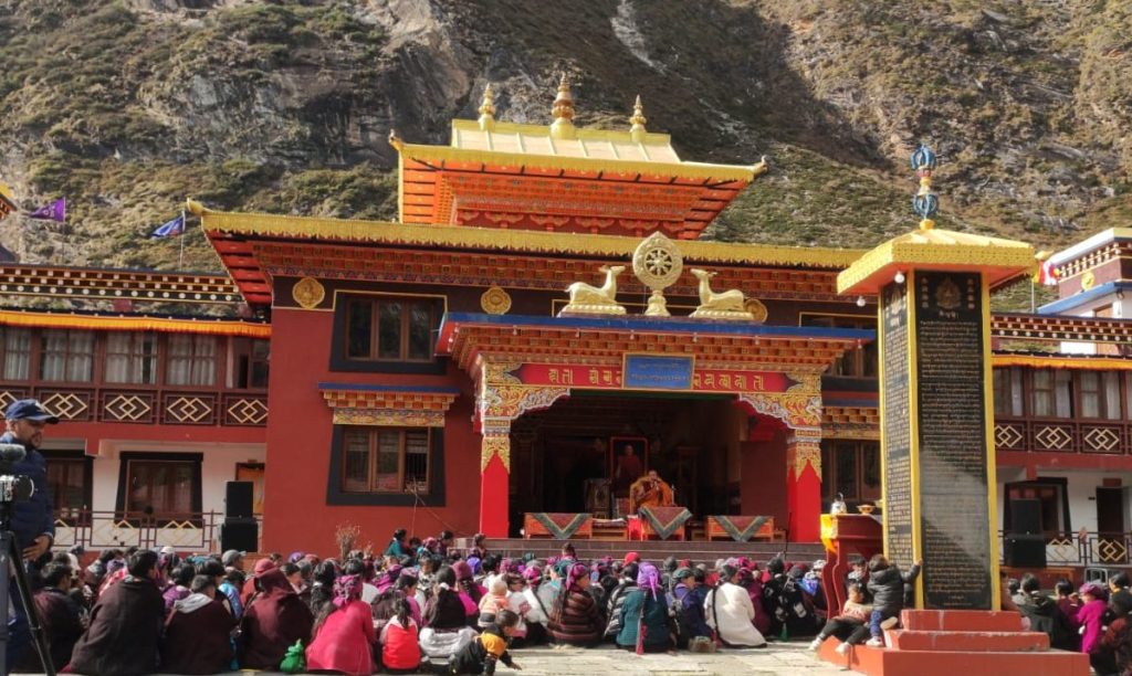 Lama Gau Monastery in the Tsum Valley trek, with devotees gathered in a courtyard, surrounded by towering rocky mountains under clear daylight