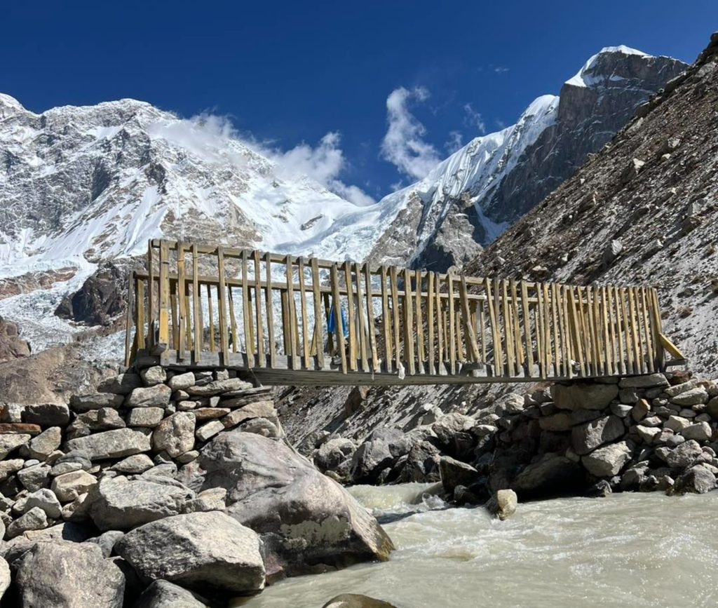 Makalu Base Camp Trek in Nepal featuring a river and small bridge with snow-capped mountains in the background – best trek in Nepal.