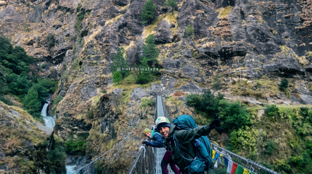 Trekkers taking photos on a hanging suspension bridge on the Manaslu Circuit Trek with a licensed guide