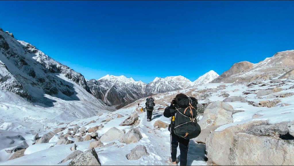 Two porters carrying heavy bags along a snowy trail on the Manaslu Circuit Trek in Nepal