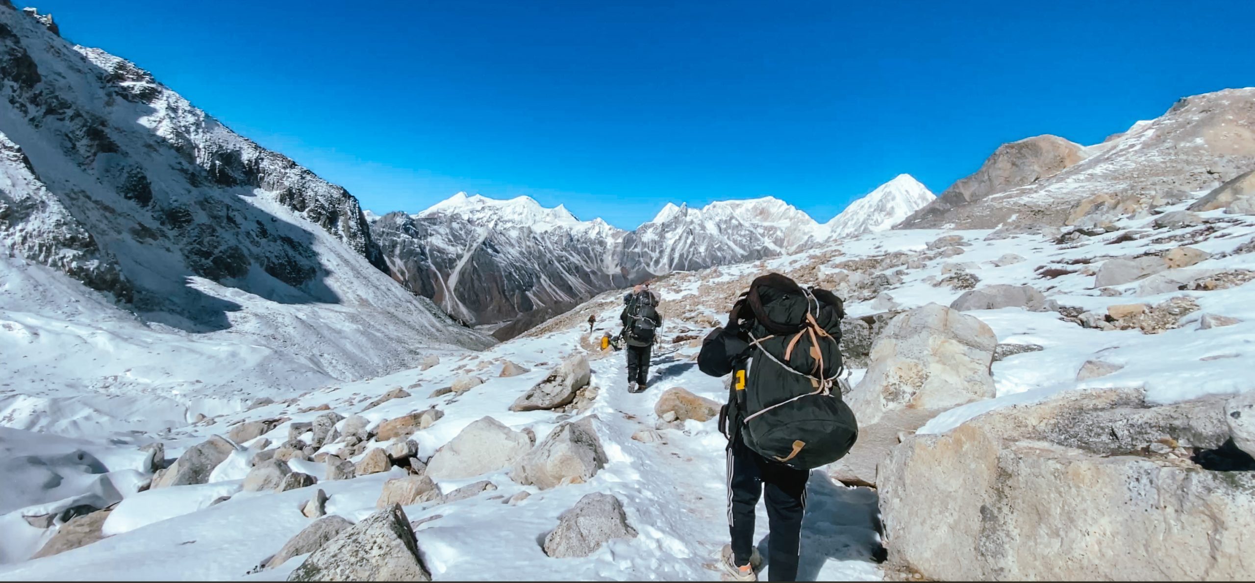 Two porters carrying heavy bags along a snowy trail, showcasing how difficult is the Manaslu Circuit Trek