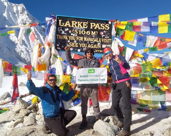 Trekkers celebrating at Larkya La Pass 5,106 m / 16,752 ft with prayer flags and snowy peaks in the background during the Manaslu Circuit Trek vs Annapurna Circuit Trek comparison journey.
