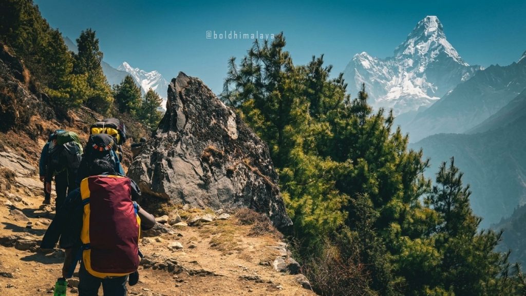 Trekkers carrying backpacks on a Himalayan trekking trail with Ama Dablam towering ahead.