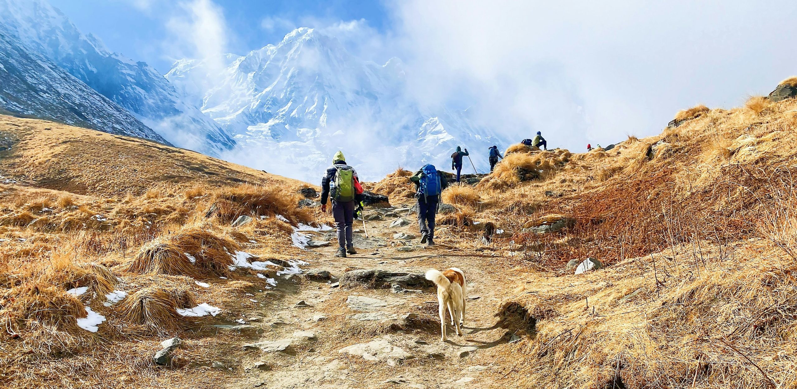 Hiring a trekking guide in Nepal as trekkers hike along a scenic Himalayan trail with snow-covered mountains in the background