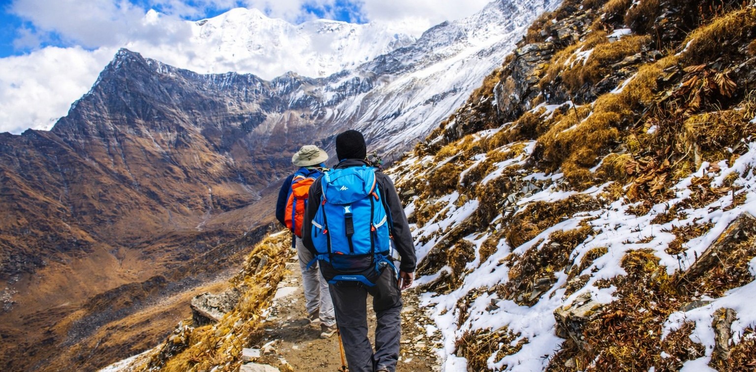 Trekking vs hiking comparison showing two trekkers with backpacks walking on a snowy Himalayan mountain trail