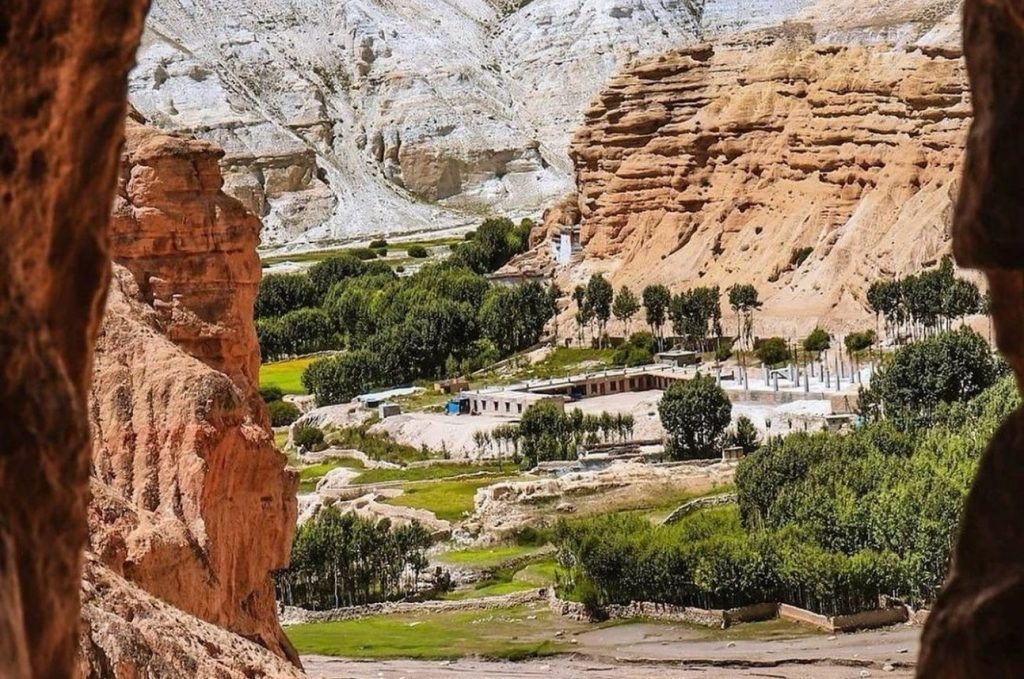 View of Upper Mustang’s dramatic desert landscape seen through a rocky cave opening, with eroded cliffs, green fields, and traditional villages