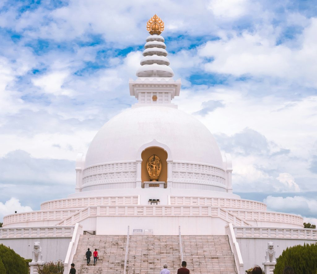 The World Peace Pagoda’s white dome rising above tree-lined pathways with blue sky: things to do in Lumbini