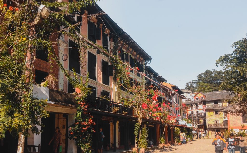 Traditional Newari houses decorated with flowers along a sunny street in Bandipur, Nepal, with people walking, a perfect highlight for any Nepal travel guide