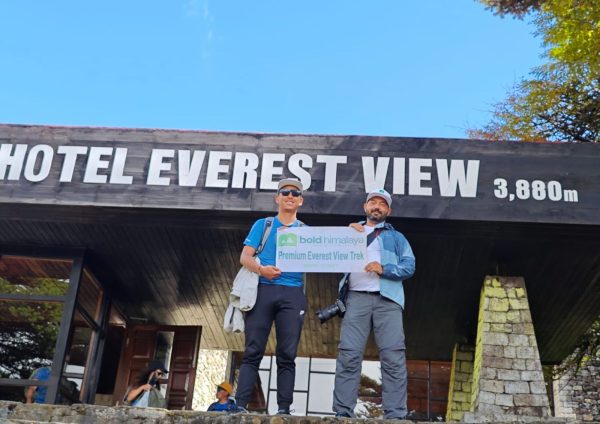Two trekkers standing in front of Hotel Everest View at 3,880 meters, holding a banner of Bold Himalaya for a premium Everest trek, representing luxury trekking in Nepal