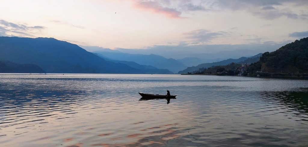 A peaceful boat floating on Phewa Lake during sunset with the Himalayan hills in the background, one of the most serene places to visit in Pokhara