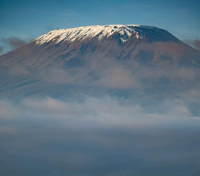 Snow-covered summit of Mount Kilimanjaro above clouds on a clear morning in Tanzania-Everest Base Camp Trek vs Kilimanjaro Climb
