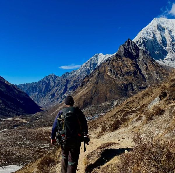 Trekker ascending Kyanjin Ri (4,773 m / 15,655 ft) with panoramic views of the Langtang Himalayas and valleys during the Langtang Valley Trek, Nepal.