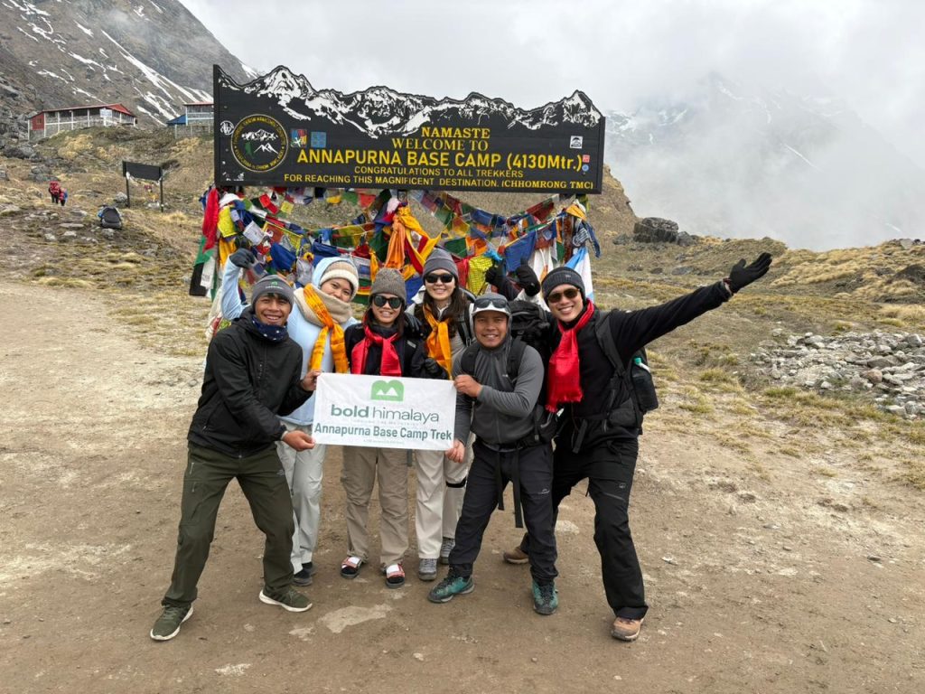 Team of Bold Himalaya, celebrating during the Annapurna Base Camp trek with panoramic Himalayan mountain views, and colorful prayer flags.