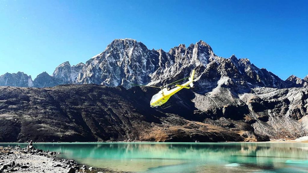 Everest Base Camp helicopter tour flying over the Himalayan mountains and a turquoise glacial lake