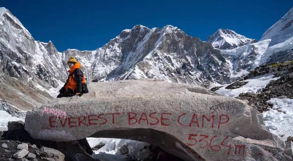 A trekker sitting on the Everest Base Camp rock marked “Everest Base Camp 5364m,” surrounded by Himalayan peaks, best monsoon treks in Nepal