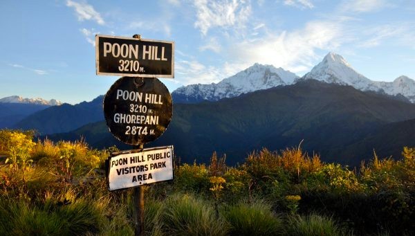 Signboard at Ghorepani Poon Hill (3,210 m) surrounded by lush green hills, alpine grass, and misty Himalayan peaks, one of the best monsoon treks in Nepal