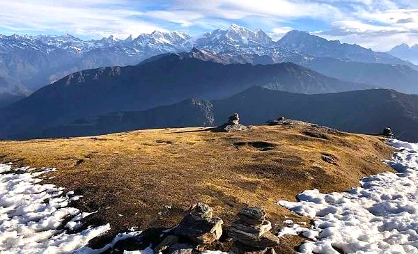 Golden alpine meadow with scattered snow patches and stone cairns at Pikey Peak, under a cloudy sky, during monsoon treks in Nepal