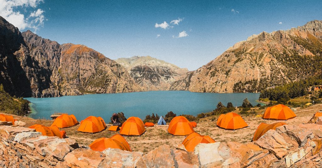 Trekking tents set up beside turquoise Shey Phoksundo Lake, surrounded by rugged mountains on the Lower Dolpo Circuit Trek, perfect for Monsoon treks in Nepal