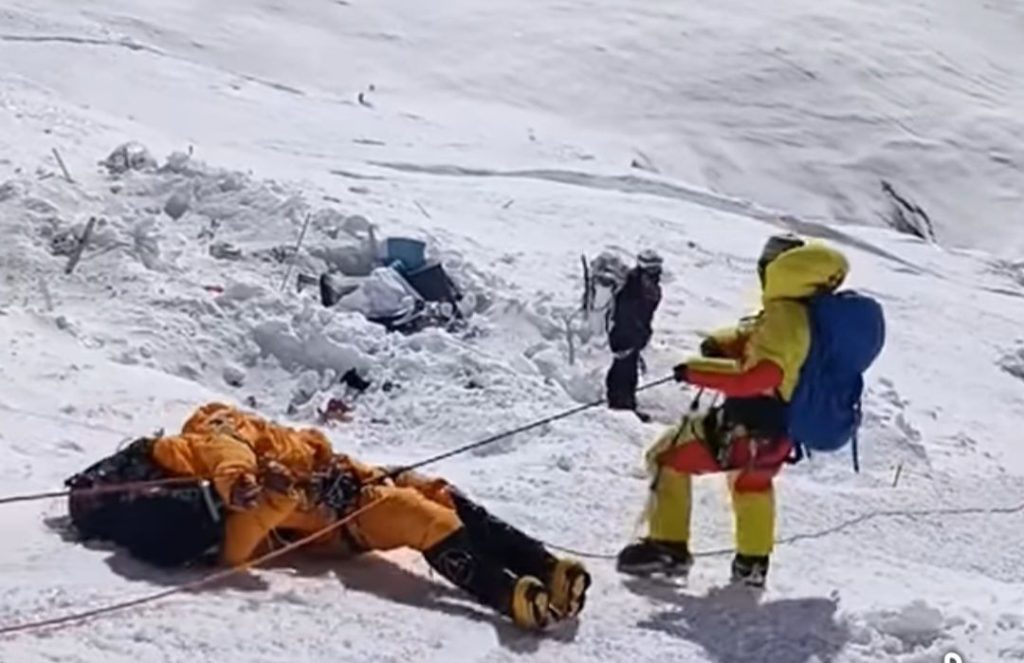 Climbers conducting a high-altitude rescue near Rainbow Valley on Mount Everest, with snow-covered terrain and an injured mountaineer being secured.