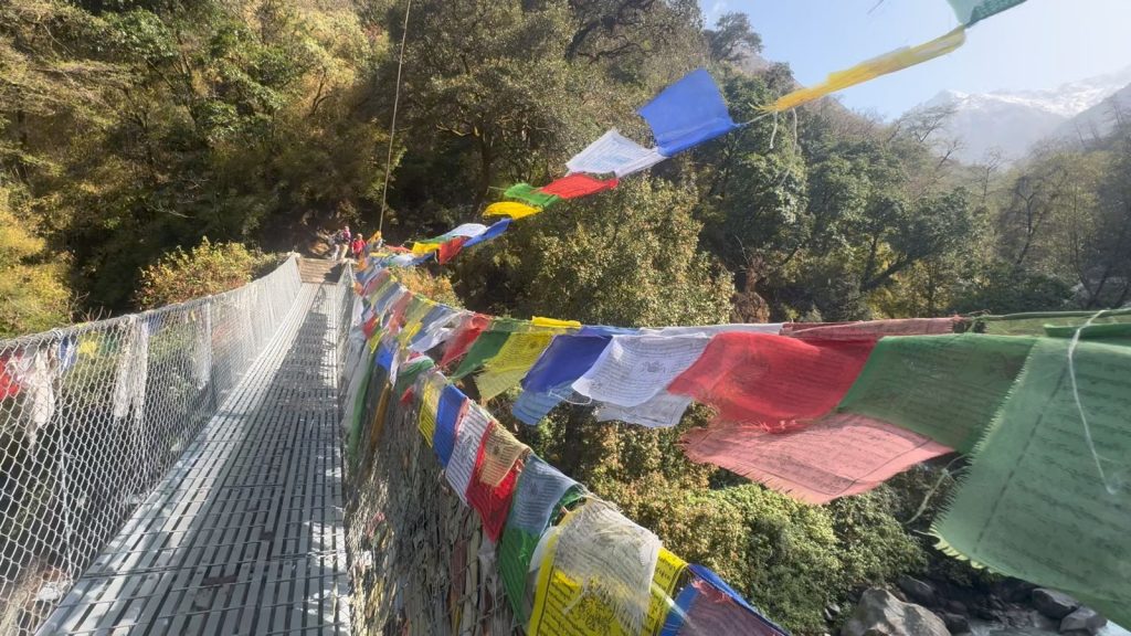 Things to know before trekking to Langtang Valley: colorful prayer flags over a suspension bridge along the scenic Himalayan trail in Nepal