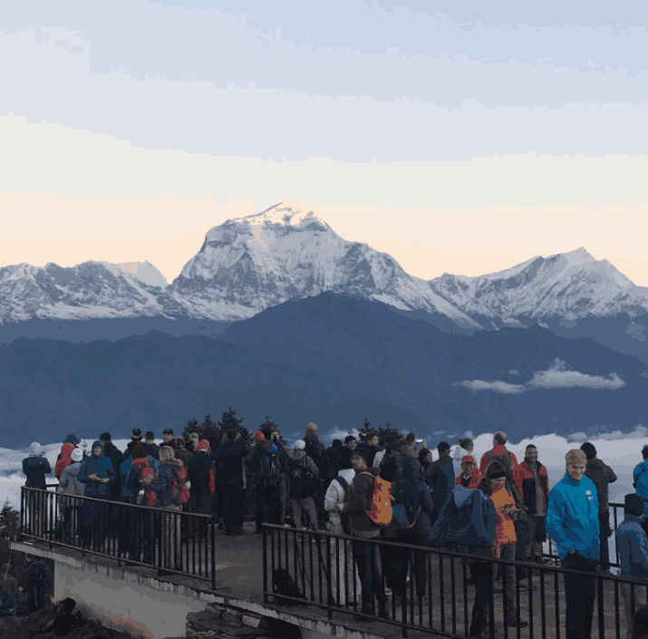 Trekkers standing on the short and easy treks, Poon Hill viewpoint platform watching the sunrise over snow-capped peaks of the Annapurna and Dhaulagiri ranges in Nepal.