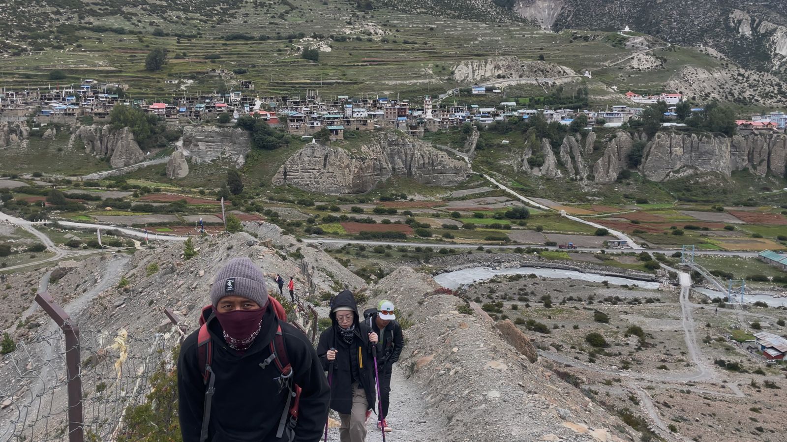 Trekkers ascending a rugged trail above Braga village on the Annapurna Circuit — a stunning mix of ancient culture and Himalayan landscapes.