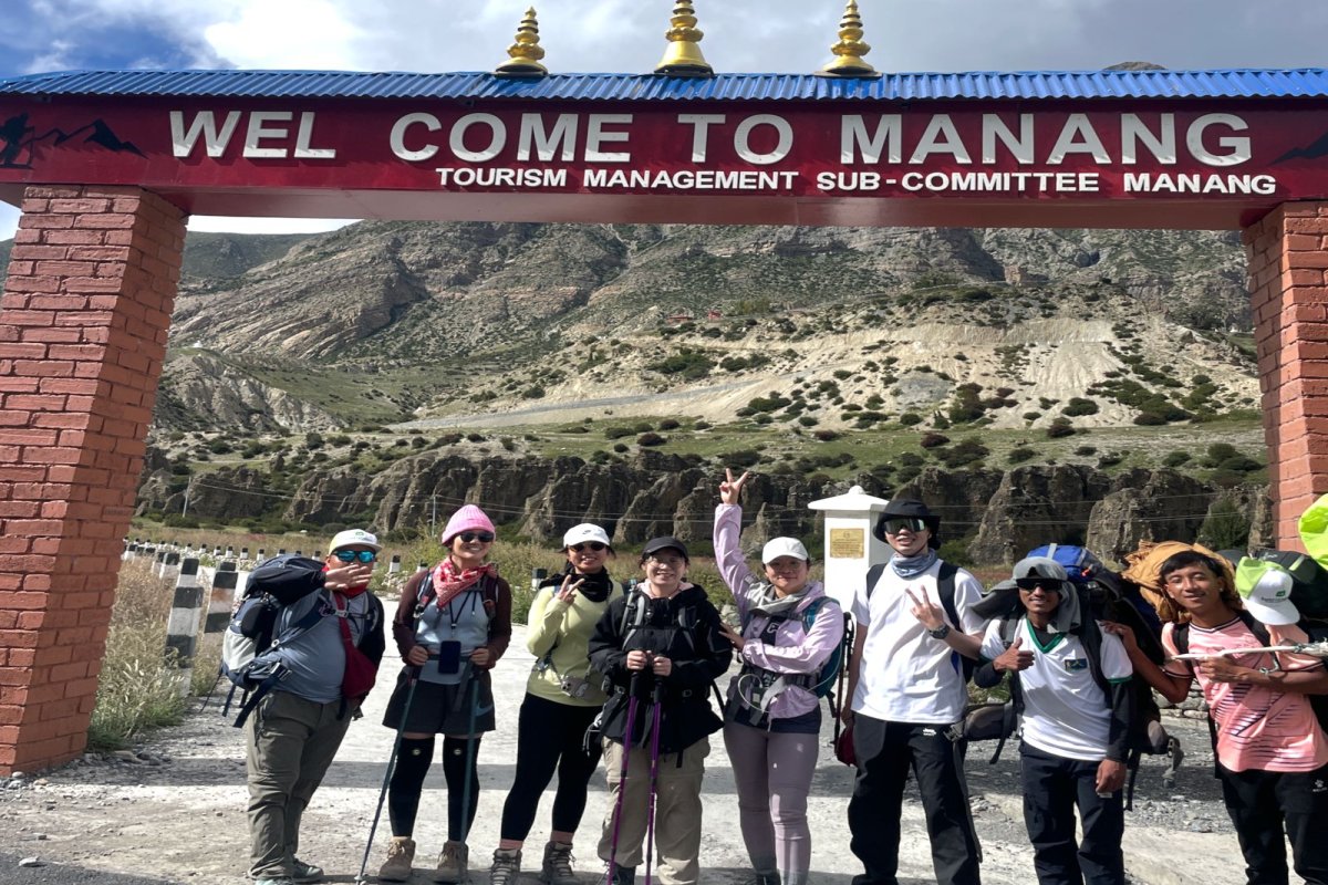 Hiker standing at the entrance gate of Manang village on Annapurna Circuit Trek with snow-capped peaks in the background
