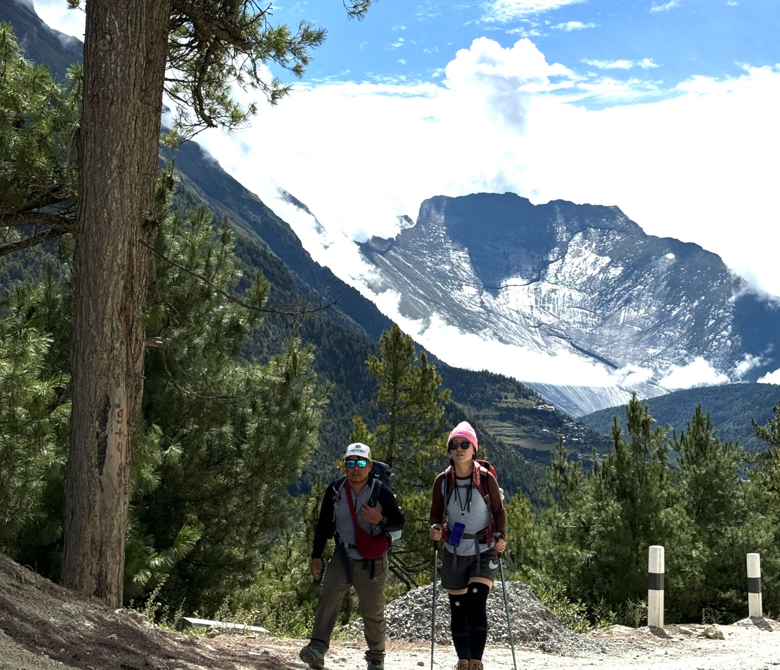 Trekker walking through pine trees on the Annapurna Circuit, with Tilicho Lake valley and snow-capped Himalayan peaks ahead