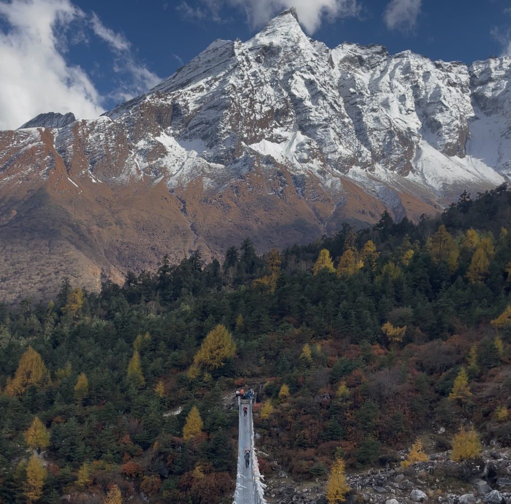 Trekkers crossing a bridge with the Manaslu Range in the background