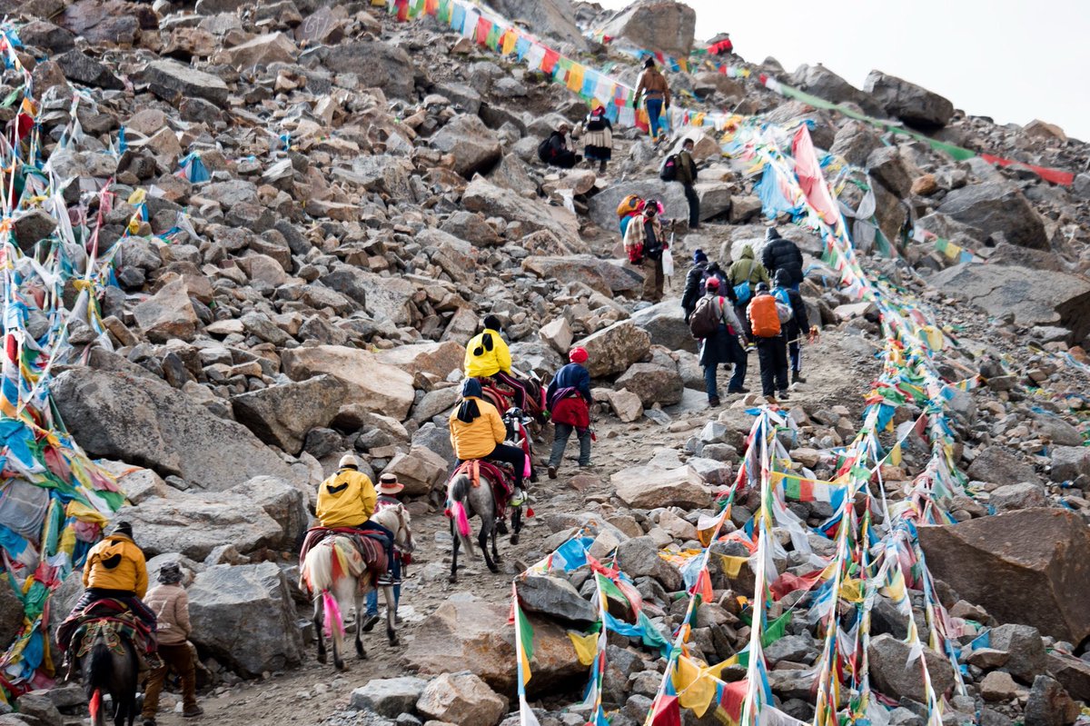 Trekkers on Mount Kailash Kora Trek climbing Dolma La Pass (5,630 m) with horses, colorful prayer flags fluttering above, high-altitude Himalayan landscape in Kailash Mansarovar Yatra.-Mount Kailash Yatra