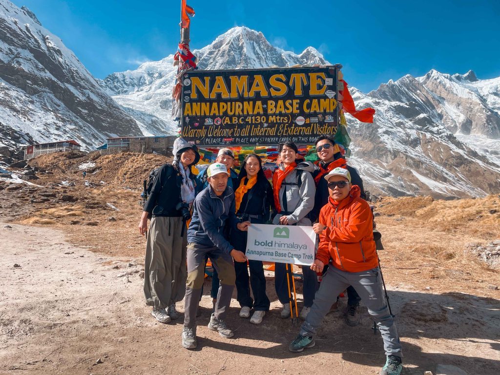 Group of trekkers posing at the welcome sign of Annapurna Base Camp (4,130 m) with snow-covered Himalayan peaks in the Annapurna Sanctuary during the Annapurna Base Camp Trek in Nepal.