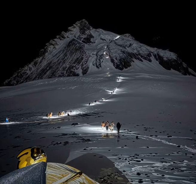 Climbers ascending Mount Everest at night with headlamps forming a glowing line on snowy slopes, illustrating Everest vs K2 climbing challenges.